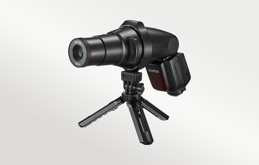 Εξάρτημα προβολής Godox AK-R21 με φλας, τοποθετημένο σε ένα μικρό μαύρο επιτραπέζιο τρίποδο