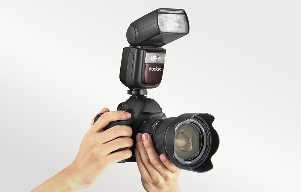 Χέρια που κρατούν μια DSLR με τοποθετημένο φλας Godox V860III και φακό