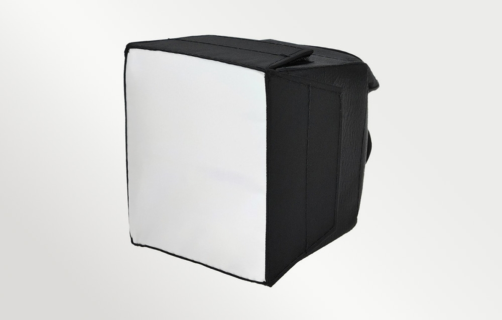 Ένας τετράγωνος, μαύρος διαχύτης τύπου softbox με λευκή επιφάνεια διάχυσης, που απεικονίζεται υπό γωνία μπροστά από ένα φωτεινό φόντο