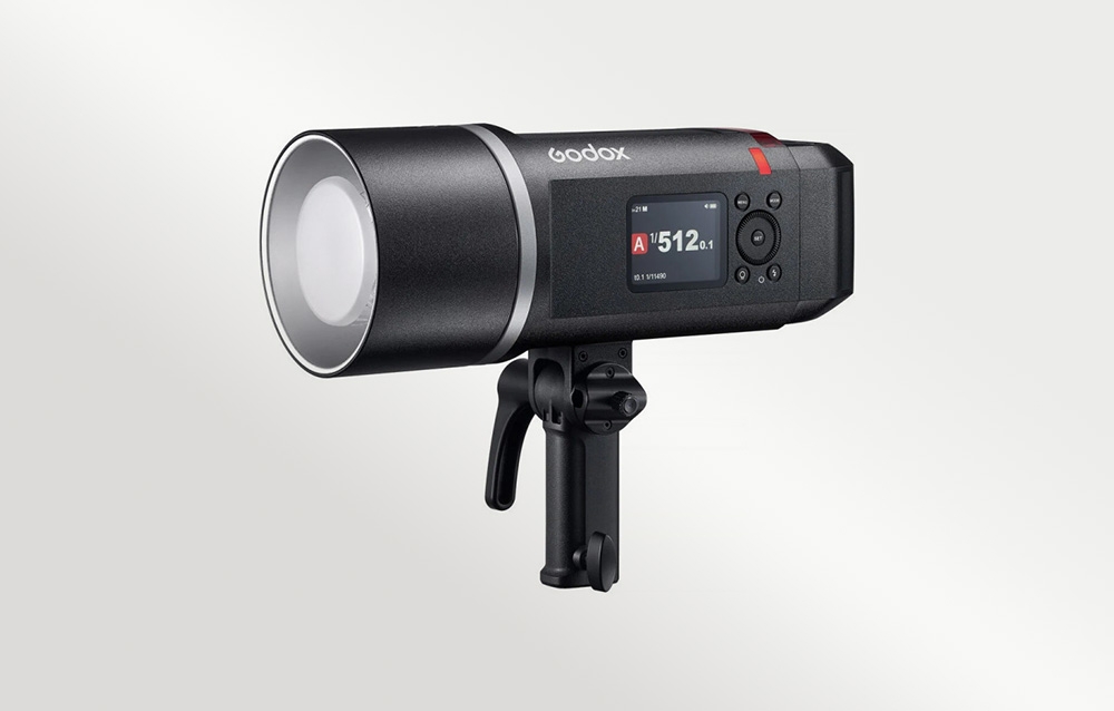 Εξωτερικό φλας Godox AD600BM II με τοποθετημένο διαχύτη και βάση τρίποδα, μπροστά από ανοιχτόχρωμο φόντο