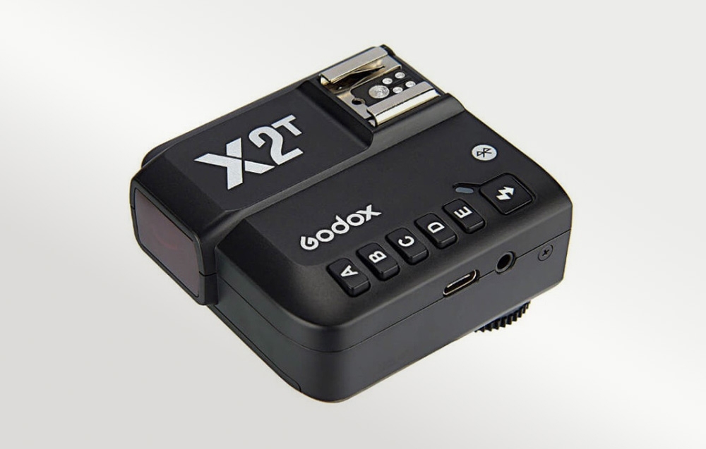 Μαύρη μονάδα Godox X2T με ορατά κουμπιά A, B, C, D και E και μεταλλική βάση σε ανοιχτόχρωμο φόντο