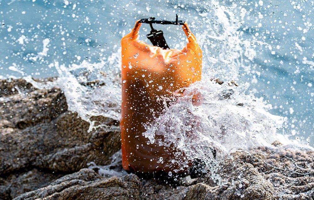 Ένα πορτοκαλί σακίδιο FunWater πάνω σε βράχους, το οποίο χτυπιέται από ένα κύμα