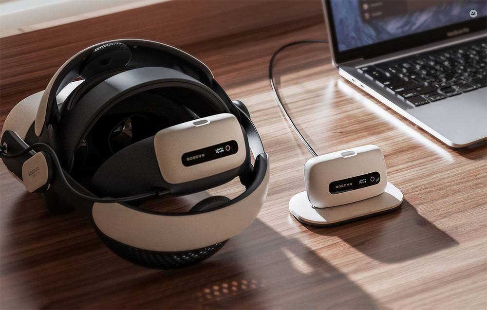 Το VR headset βρίσκεται πάνω σε ένα γραφείο· μία μπαταρία είναι συνδεδεμένη στο λουράκι κεφαλής, ενώ η άλλη βρίσκεται δίπλα της στον σταθμό φόρτισης.