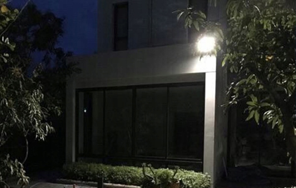 Ένας μαύρος προβολέας LED τοποθετημένος πάνω από τον γυάλινο τοίχο της κατοικίας, που φωτίζει την είσοδο μετά το σούρουπο