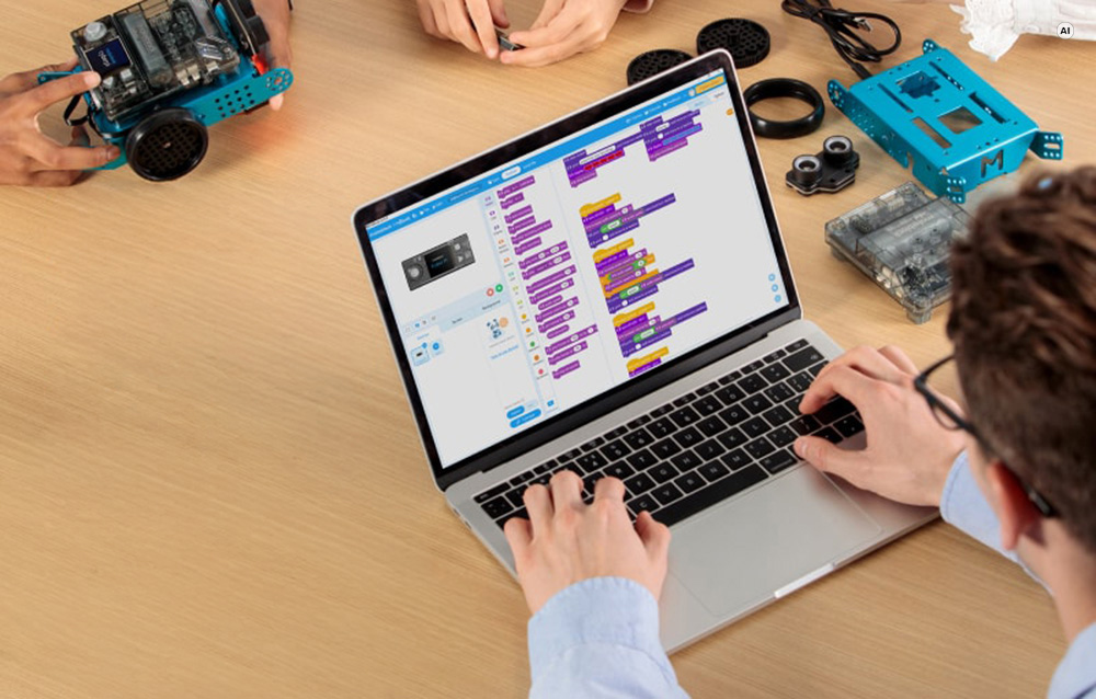 Ένα άτομο που προγραμματίζει ένα ρομπότ Makeblock mBot2 σε φορητό υπολογιστή χρησιμοποιώντας ειδικό λογισμικό, δίπλα στα εξαρτήματα του κιτ