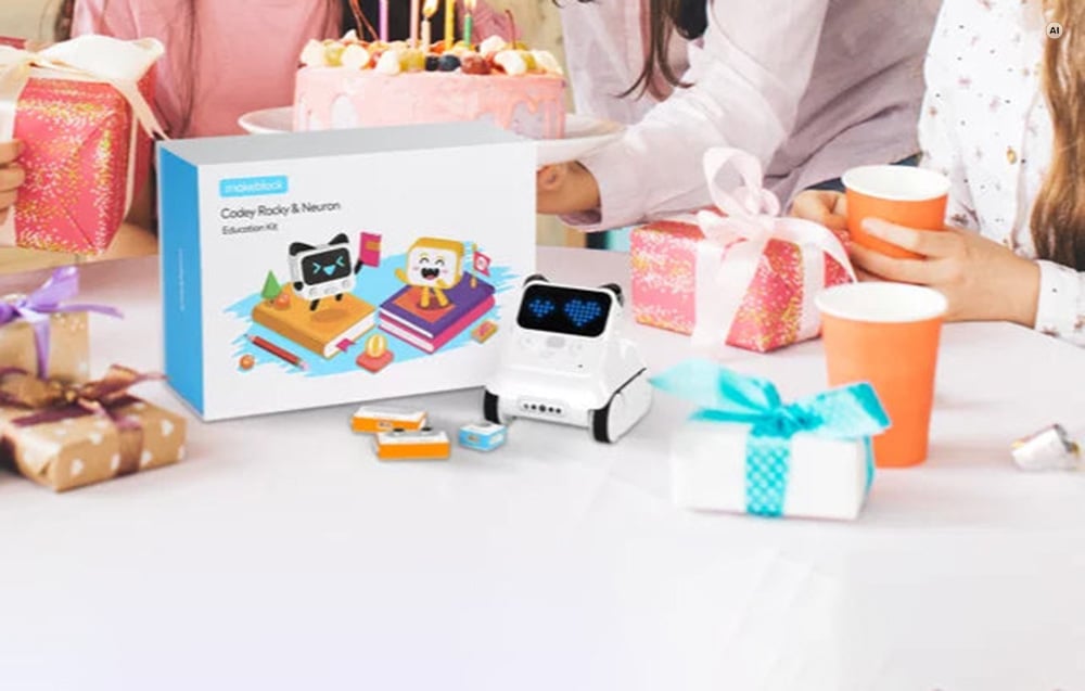 Ένα ρομπότ Makeblock Codey Rocky, η συσκευασία του και δώρα γενεθλίων βρίσκονται πάνω στο τραπέζι δίπλα στην τούρτα