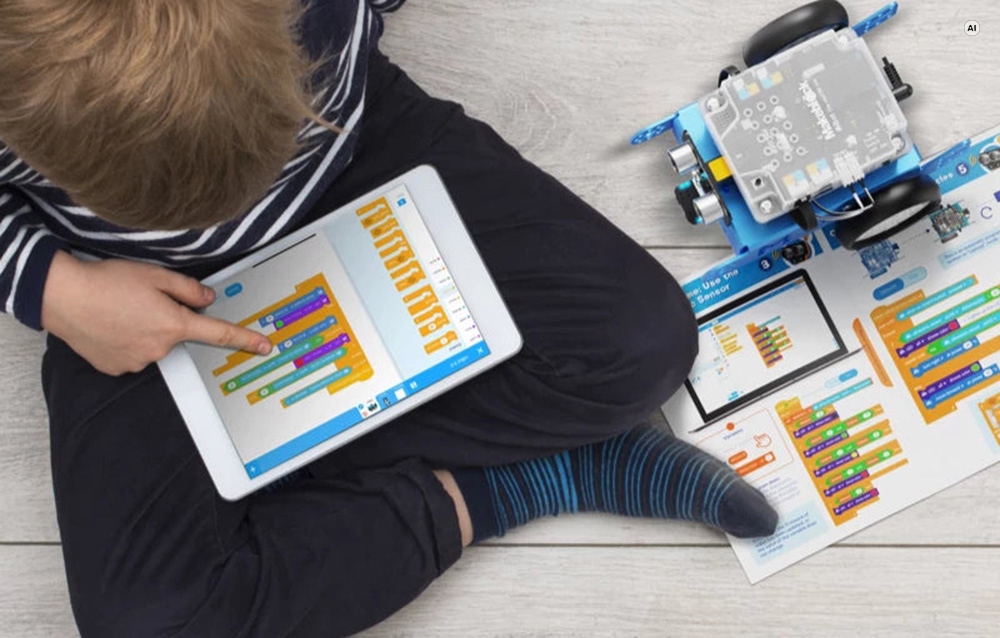Ένα αγόρι προγραμματίζει το ρομπότ Makeblock mBot σε tablet· το ρομπότ βρίσκεται στο πάτωμα δίπλα στο εγχειρίδιο