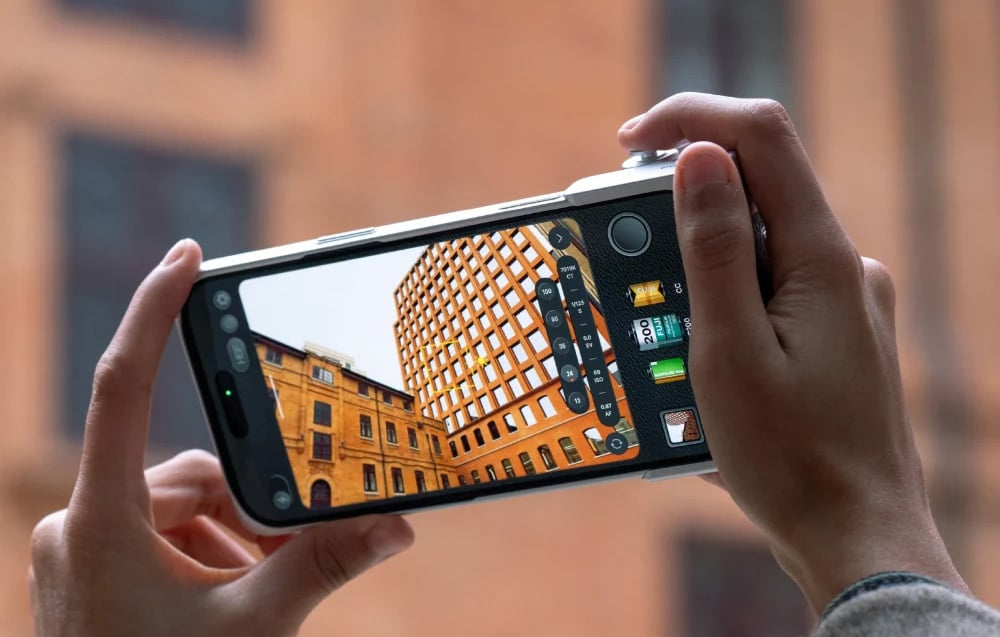 Χέρια που κρατούν ένα smartphone σε θήκη κάμερας ενώ φωτογραφίζουν ένα πορτοκαλί κτίριο· το πλαίσιο είναι ορατό στην οθόνη.