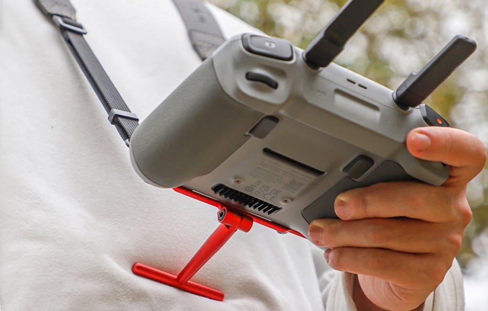 Mężczyzna korzystający με έλεγχο DJI.  Czerwony uchwyt Sunnylife αστείο opparty o jego brzuch.