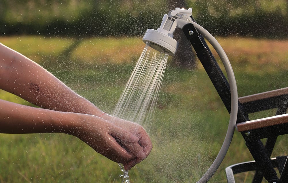 Το φορητό ντους Flextail Max Shower τοποθετημένο σε ένα παγκάκι κατά το πλύσιμο των χεριών σε εξωτερικό χώρο.