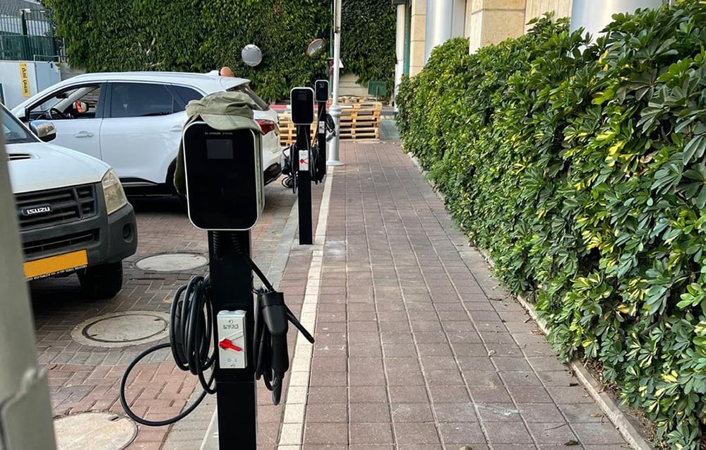 Ένας αυτόνομος σταθμός φόρτισης ηλεκτρικών αυτοκινήτων που βρίσκεται κοντά σε υπαίθριες θέσεις στάθμευσης.