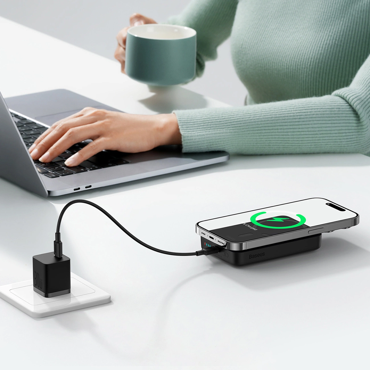 Το Powerbank Baseus Magnetic Mini σε περιβάλλον γραφείου βρίσκεται δίπλα στο φορητό υπολογιστή στο γραφείο και συνδέεται με την πρίζα μέσω καλωδίου και υπάρχει ένα τηλέφωνο σε αυτό που φορτίζεται.