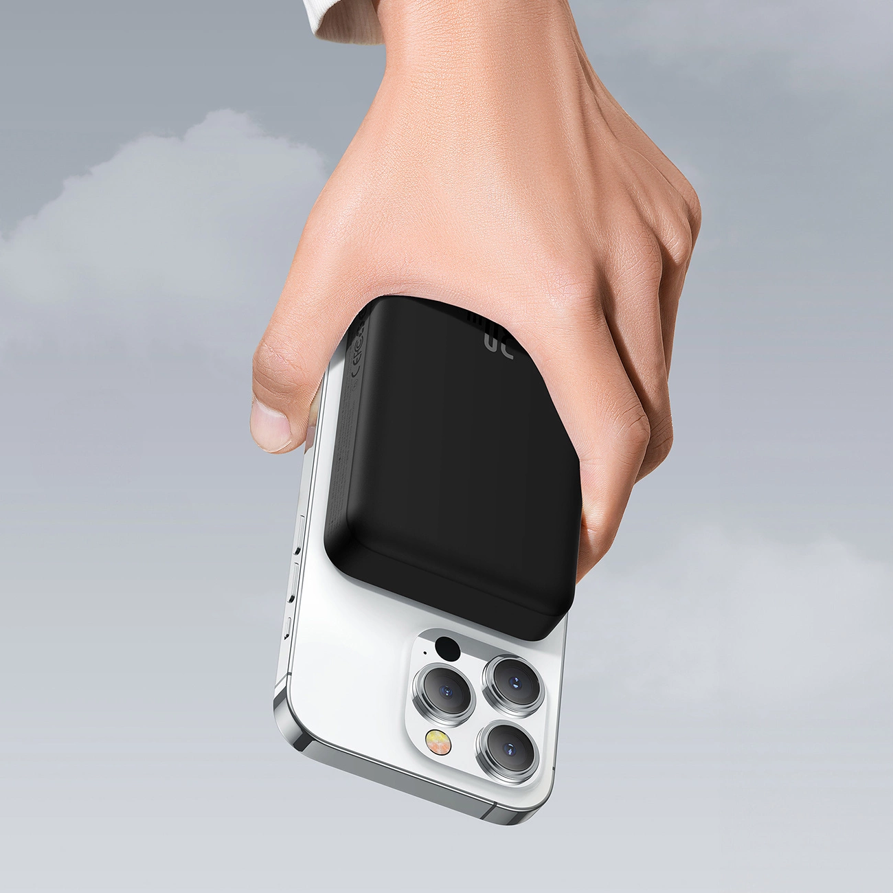 Ένα χέρι που κρατά ένα τηλέφωνο με ένα Baseus Magnetic Mini induction Powerbank 10000mAh 30W συνδεδεμένο στο φόντο των σύννεφων