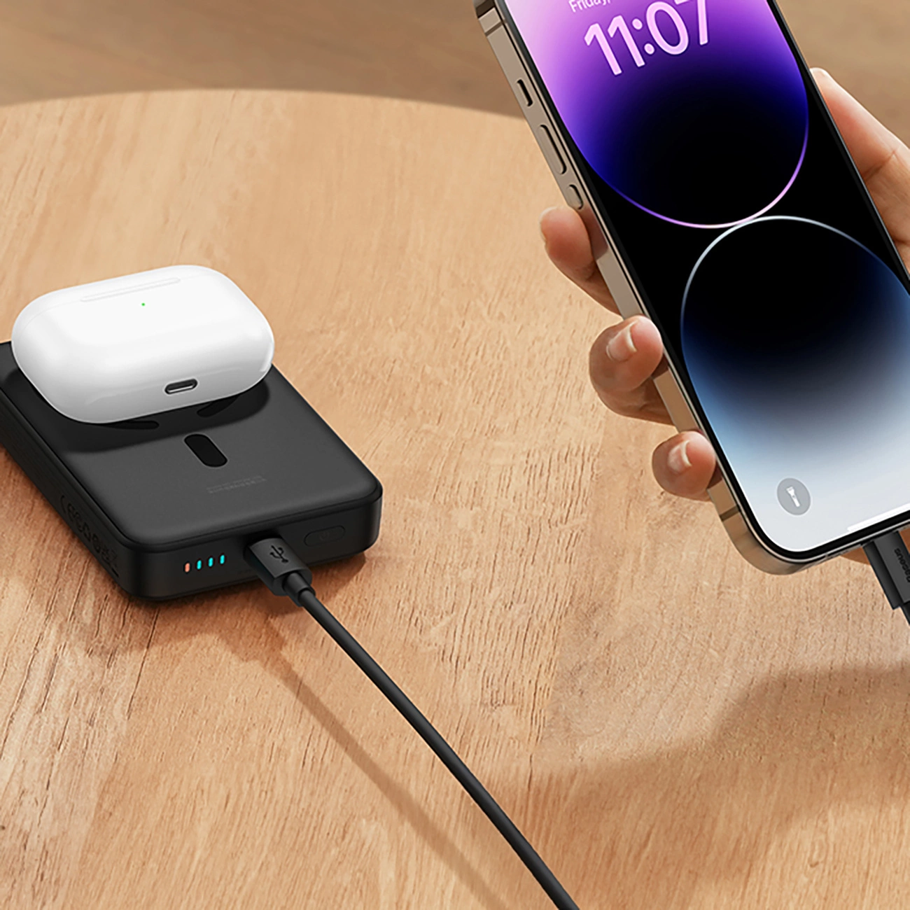 Το Baseus Magnetic Mini επαγωγικό Powerbank 10000mAh 30W βρίσκεται σε ένα ξύλινο τραπέζι στο οποίο είναι συνδεδεμένο το τηλέφωνο μέσω καλωδίου και τα ακουστικά επαγωγικής φόρτισης βρίσκονται στην επιφάνεια του Baseus Magnetic Mini Powerbank.
